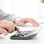 Quanto Custa um Inventário em 2026? Advogado calculando custos de inventário em Praia Grande SP utilizando calculadora e documentos sobre mesa de escritório.